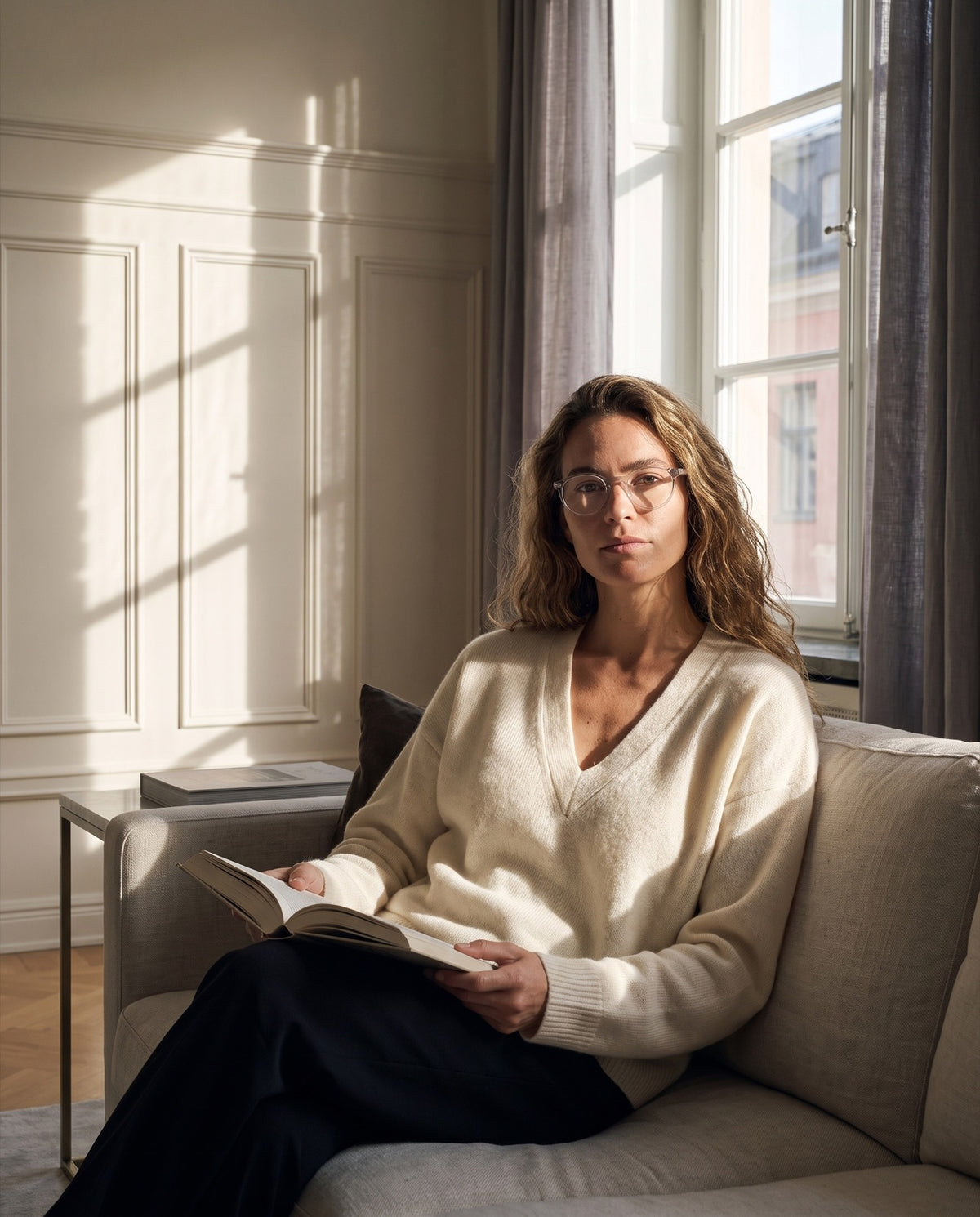 Eine Frau liest auf dem Sofa im tiefen Septemberlicht, mit der Lesebrille Emily Quartz.
